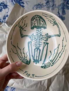 a hand holding a bowl with a skeleton design on the bottom and green paint over it