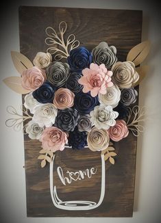 a mason jar filled with paper flowers on top of a wooden sign that says home