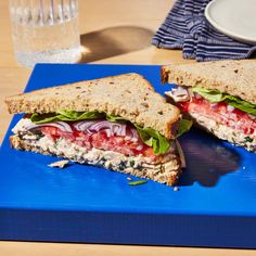 a cut in half sandwich sitting on top of a blue cutting board next to a glass of water