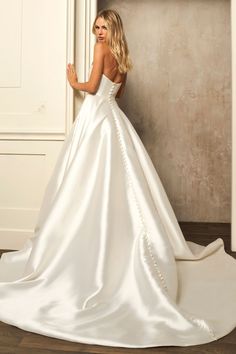 a woman in a white wedding dress leaning against a wall with her back to the camera