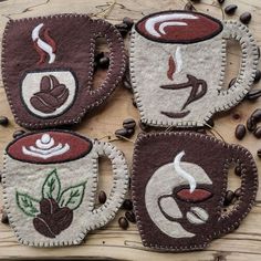 four coffee mug cozies are sitting on top of a wooden table with coffee beans around them