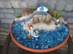 a potted planter filled with blue glass pebbles and little mermaid figurines