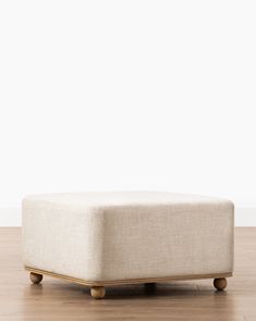 a white ottoman sitting on top of a hard wood floor in front of a white wall