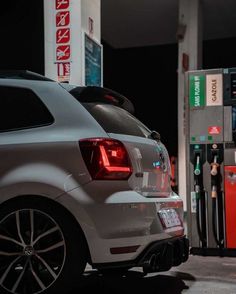 the back end of a white car at a gas station with an attendant filling it up