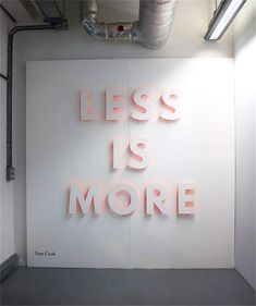 the words less is more are lit up against a white wall