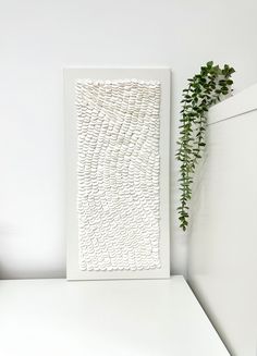 a plant is sitting on a shelf next to a white framed art piece with wavy lines