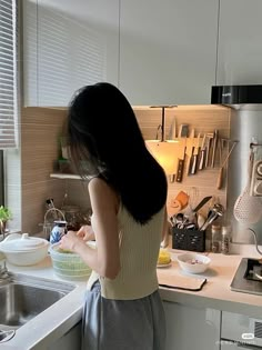 a woman standing in a kitchen next to a sink and counter top with utensils on it