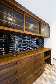 a vase with flowers on top of a wooden dresser next to a brick tiled wall