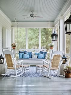 a porch with white rocking chairs, blue pillows and lanterns on the front porch area