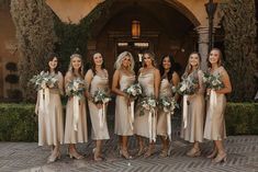 a group of women standing next to each other in front of a building holding bouquets