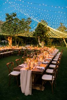 a long table with white linens and candles is set up for an outdoor dinner