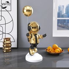 a small gold astronaut figurine is on a table next to oranges and a bowl of fruit