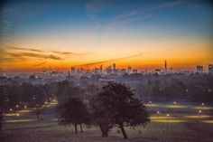 the sun is setting over a city with trees in the foreground and buildings in the background