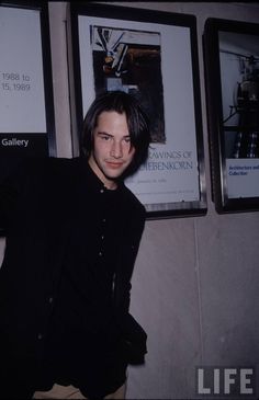 a man leaning against a wall with posters behind him