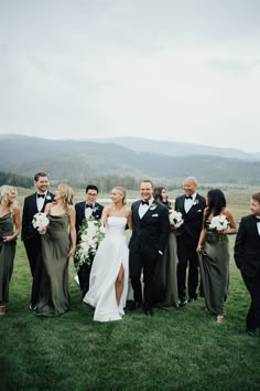 a group of people in formal wear posing for a photo on the grass with mountains in the background