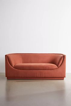 an orange couch sitting on top of a floor next to a white wall with a plant in it