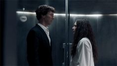 a man and woman standing next to each other in front of a glass elevator door