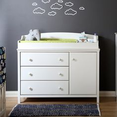 a baby's room with a crib, dresser and wall decal in the shape of clouds