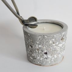 a candle that is sitting inside of a cement container with scissors sticking out of it