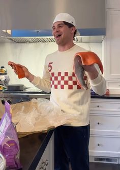 a man in a kitchen holding an orange object and wearing a white hat with the number five on it