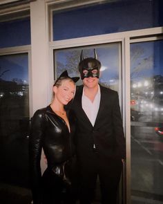 a man and woman dressed up as batman and catwoman pose for a photo in front of a window