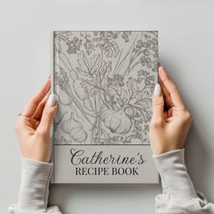 two hands are holding the cover of a recipe book with flowers on it and text that reads, catherine's recipe book