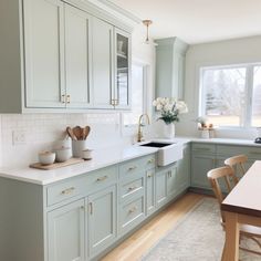 a kitchen filled with lots of green cabinets and white counter tops next to a dining room table