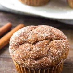 a close up of a muffin on a wooden table with cinnamon sticks in the background