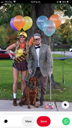 a man and woman standing next to a dog with balloons on their heads, in front of a tree