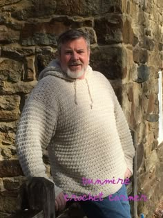 a man standing next to a stone building wearing a white knitted sweater and blue jeans