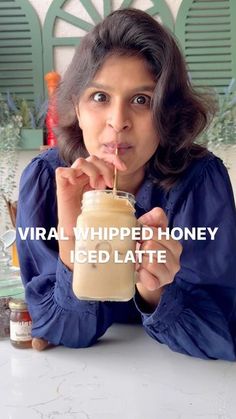 a woman sitting at a table with a drink in her hand and the words virtual whipped honey iced latte