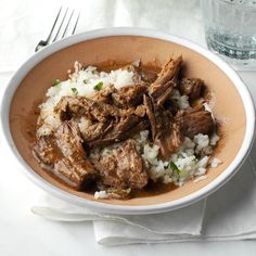 a bowl filled with meat and rice next to a glass of water on a table