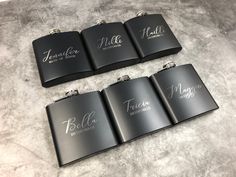 four black flasks with the names of five different brands on them sitting on a table