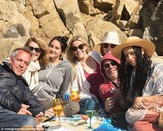 a group of people sitting next to each other on top of a sandy beach covered in rocks