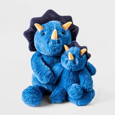 two blue stuffed animals sitting next to each other on a white surface with one holding the other's head