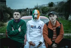 three young men sitting next to each other in front of a car with their faces painted like the irish flag