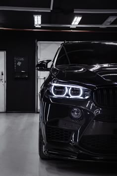 the front end of a black bmw car in a garage with its lights turned on