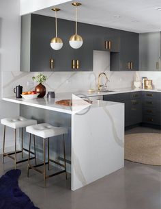 a modern kitchen with marble counter tops and gold pendant lights hanging from the ceiling over the island