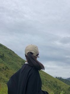 a woman standing on top of a lush green hillside next to a hill covered in grass