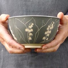 a person holding a bowl in their hands with white flowers on the front and side