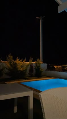 an empty pool at night next to a white table and chair with blue lights on it