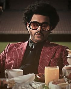 a man in a red suit and sunglasses sitting at a table with food on it