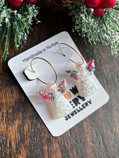 the earrings are decorated with colorful flowers and glittery angel wings, on top of a wooden table