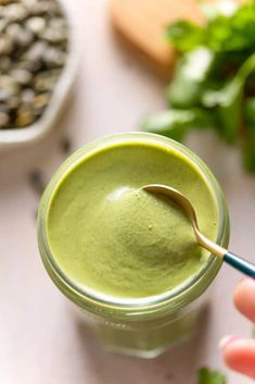 a hand holding a spoon over a green smoothie