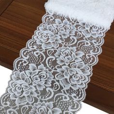 a white lace with flowers on it is laying on a wooden table next to a piece of wood