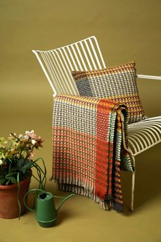 a chair with a blanket on it next to a potted plant and watering can