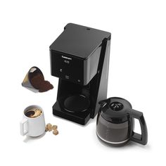 a black coffee maker next to a cup of coffee and some other items on a white surface