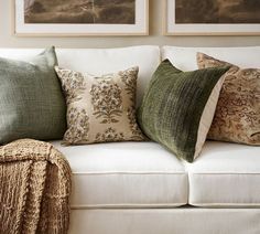 a white couch with pillows on top of it next to two pictures hanging above the couch