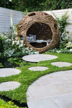 an outdoor garden with stepping stones, grass and a circular wicker bed in the middle