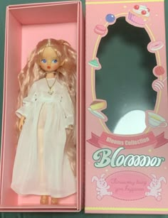 a doll in a pink box with a white dress on it's body and blonde hair